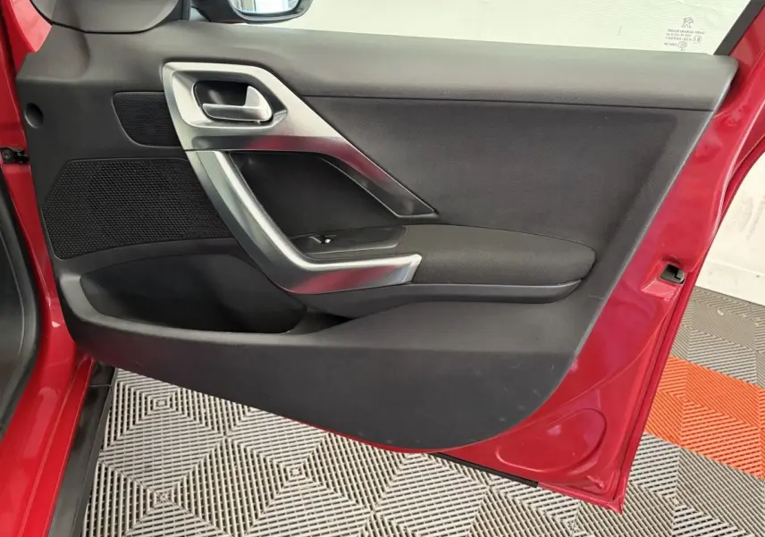Vue rapprochée de la porte avant gauche rouge du Peugeot 2008 avec poignée argentée et panneau noir.