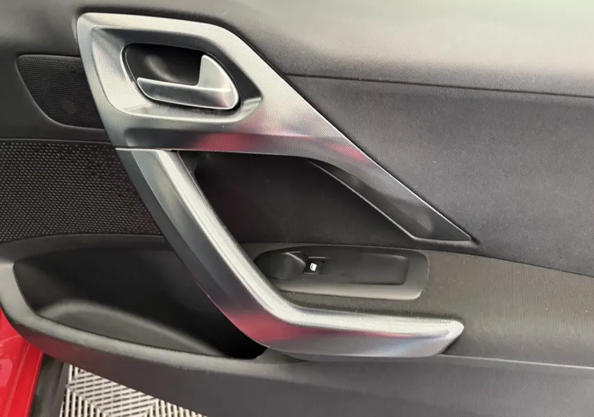 Poignée intérieure côté gauche de la porte rouge d'un Peugeot 2008 Puretech 110 Allure, avec insert gris métallique.