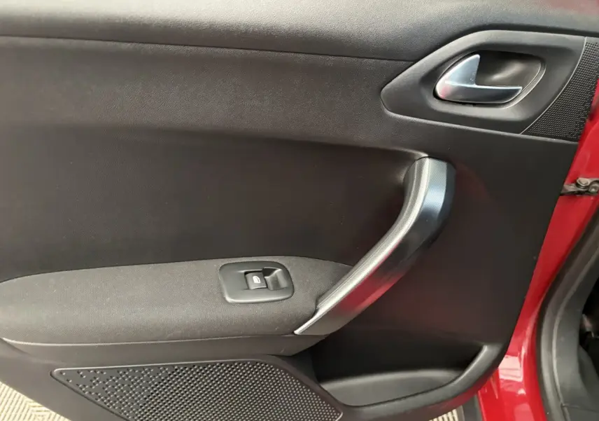 Gros plan sur la porte intérieure côté gauche d'une Peugeot 2008 rouge, avec poignée argentée et bouton de fenêtre électrique.