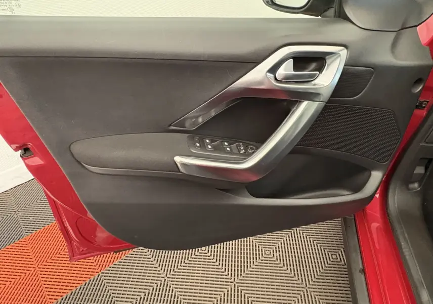 Vue rapprochée de la porte avant gauche rouge du Peugeot 2008 avec garniture noire et poignée argentée.