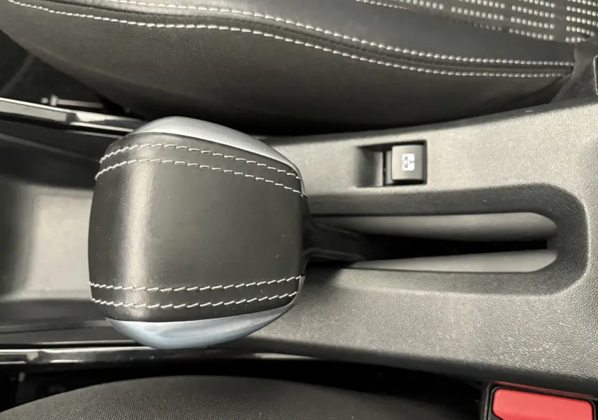 Gros plan sur le levier de vitesse en cuir noir avec surpiqûres blanches dans l'habitacle d'un Peugeot 2008 rouge.