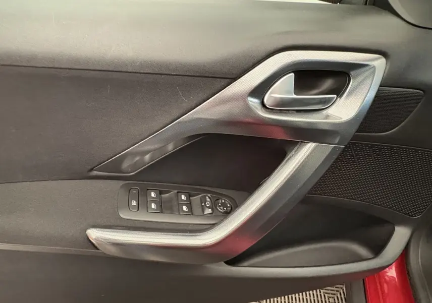 Vue rapprochée de la porte côté conducteur rouge du Peugeot 2008 avec commandes des vitres et poignée argentée.