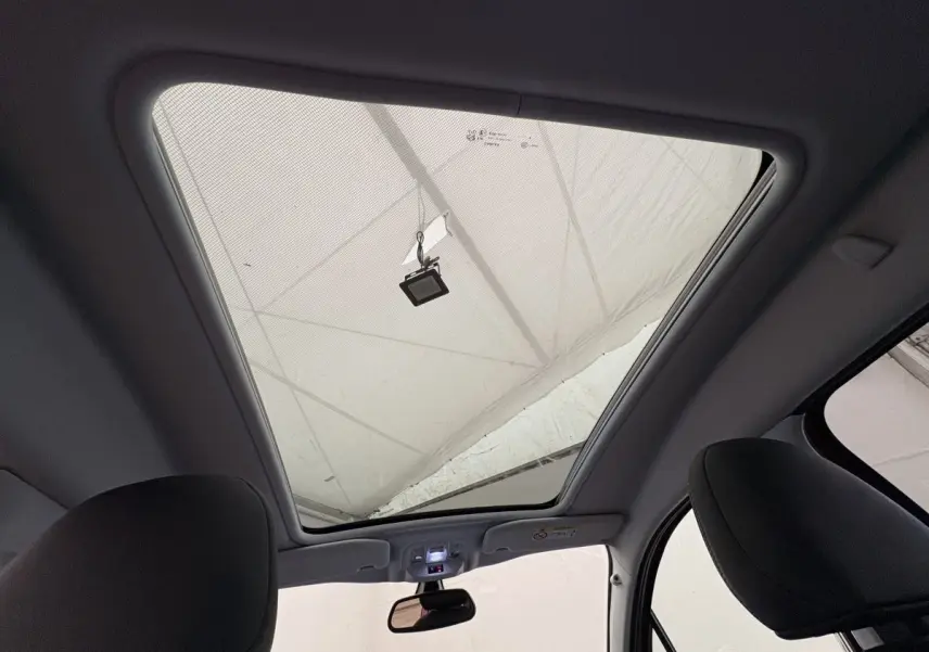 Toit panoramique vu de l'intérieur avant du Peugeot 2008 rouge, mettant en valeur le grand vitrage et les sièges noirs.