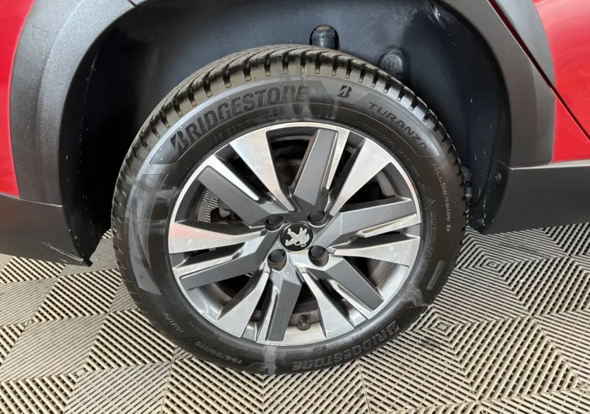 Gros plan sur la roue avant droite d’un Peugeot 2008 rouge, avec jante alliage et pneu Bridgestone Turanza.