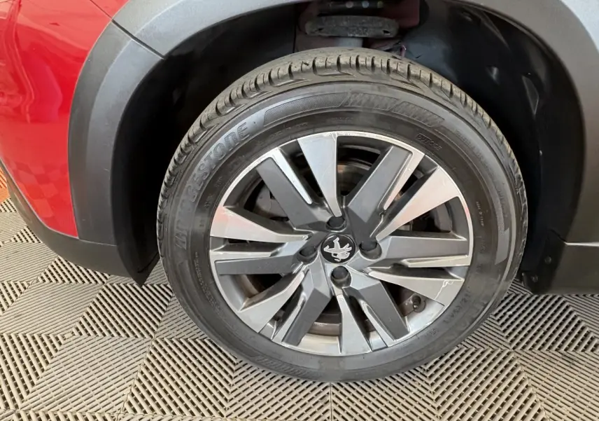 Gros plan sur la roue avant gauche rouge d’un Peugeot 2008 avec jante alliage et logo lion central.