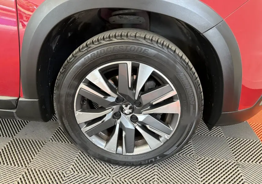 Gros plan sur la roue avant gauche d'un Peugeot 2008 rouge, mettant en valeur la jante alliage et le pneu Bridgestone.