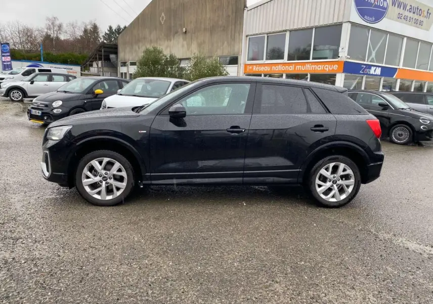 Audi Q2 noire vue de profil côté gauche, avec jantes alliage et carrosserie brillante sous la pluie.