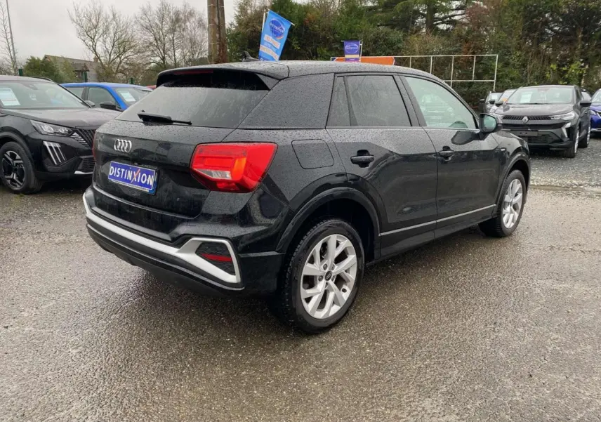 Audi Q2 noir vue 3/4 arrière droit, hayon électrique et jantes alliage visibles sous un ciel couvert.