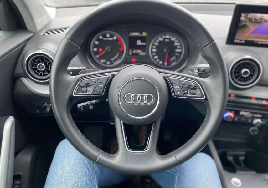 Vue centrée sur le volant noir de l'Audi Q2 2023, avec tableau de bord et écran de caméra de recul visibles.