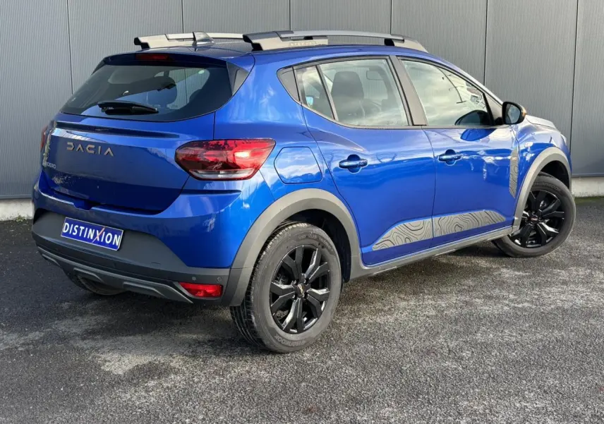 Vue 3/4 arrière droite du Dacia Sandero Stepway Eco-G 100 Extrême Bleu Iron avec jantes noires et barres de toit grises.