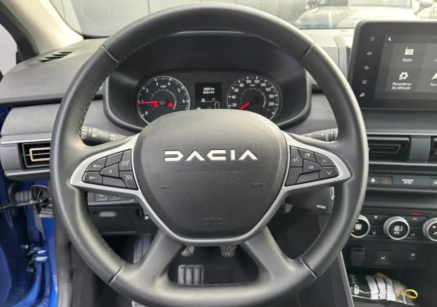 Vue intérieure centrée sur le volant noir Dacia avec tableau de bord et écran tactile du Dacia Sandero Stepway Bleu Iron 2025.