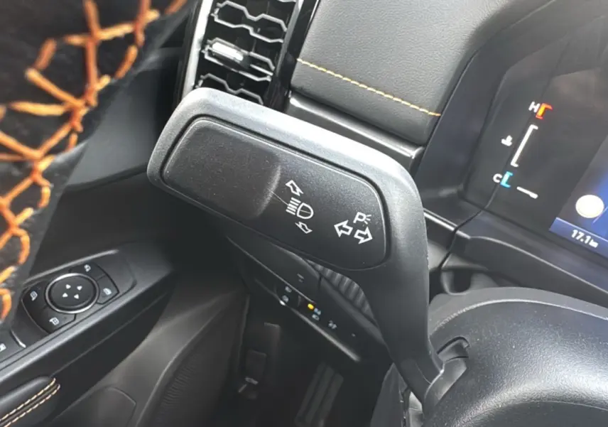 Gros plan sur la manette de clignotants et les commandes au volant avec surpiqûres orange dans l’habitacle noir du Ford Ranger Wildtrak.