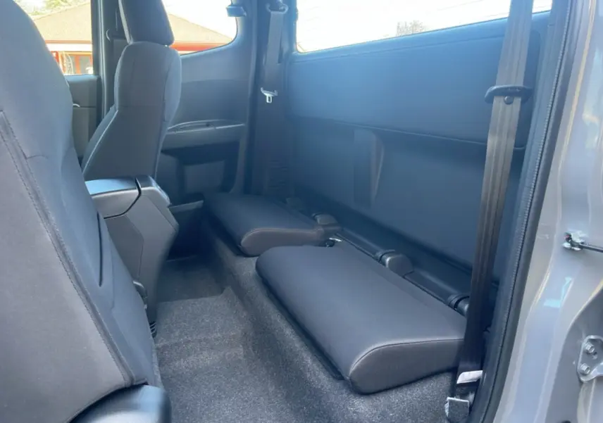 Vue intérieure arrière droite du pick-up Isuzu D-MAX 2026 gris Kinabalu avec sièges strapontins rabattus en tissu noir.