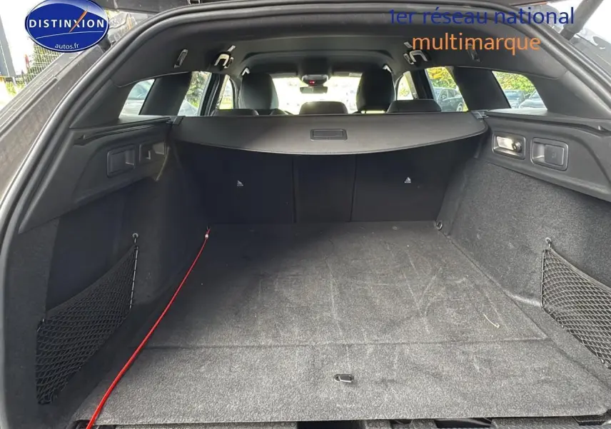 Coffre ouvert vu de l'arrière d'une Peugeot 308 SW PHEV 225 GT gris selenium avec filet de rangement latéral.