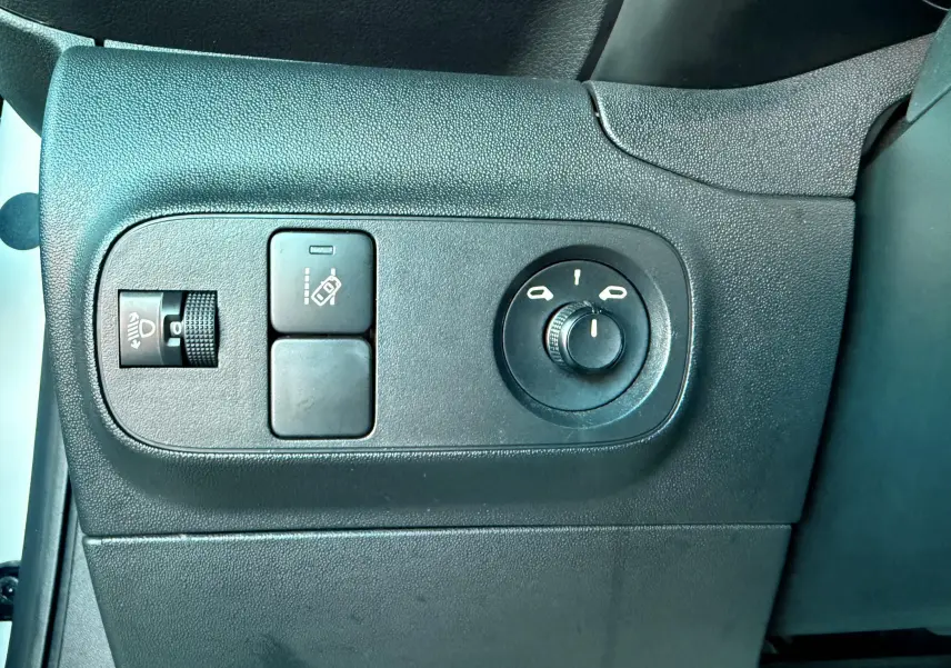 Gros plan sur les commandes de réglage des rétroviseurs et des phares du tableau de bord côté conducteur d'une Citroën C3 blanche.