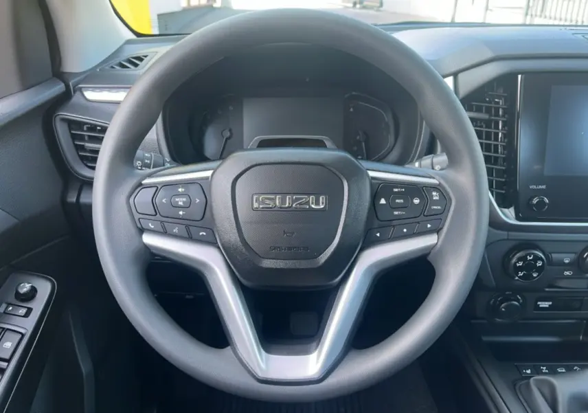 Vue rapprochée du volant multifonctions ISUZU D-MAX 2026 avec tableau de bord et écran tactile à droite.