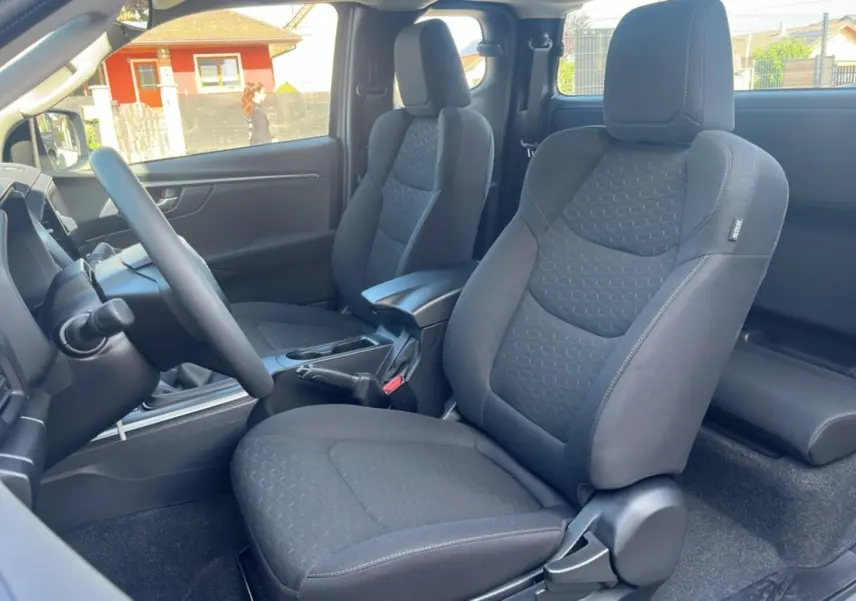 Vue intérieure côté conducteur de l’Isuzu D-MAX 2026 avec sièges tissu gris foncé et accoudoir central avant.