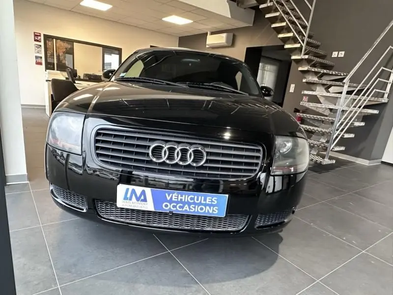 Audi TT Coupé noir 2002 vue de face en intérieur, avec calandre distinctive et plaque "Véhicules Occasions".