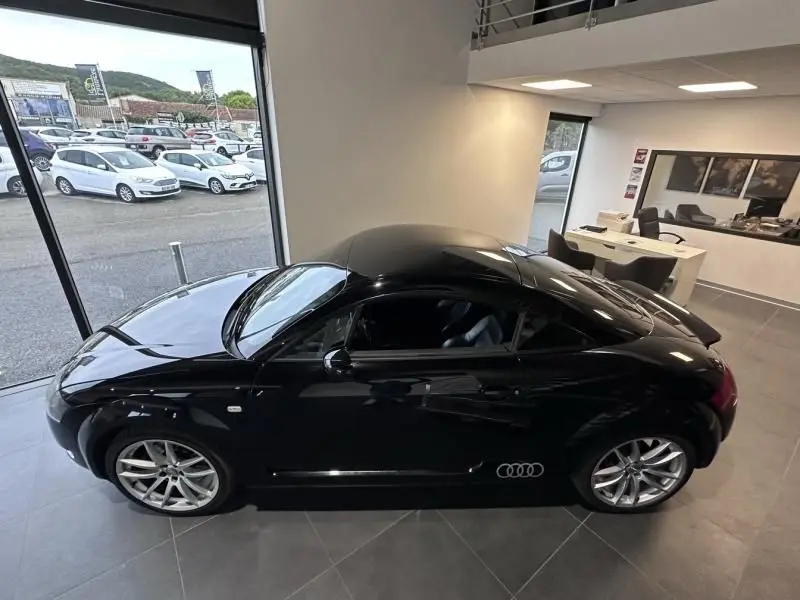 Audi TT Coupé noir de 2002 vu de profil côté gauche, avec jantes alliage et intérieur visible en showroom.