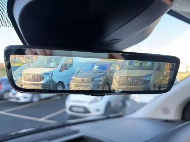 Vue dans le rétroviseur intérieur montrant un Peugeot Expert Fourgon noir de face, stationné parmi d'autres véhicules.