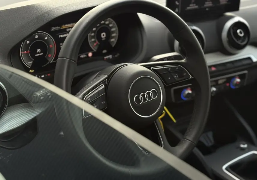 Vue intérieure rapprochée du volant cuir multifonction de l’Audi Q2 30 TDI S-Line avec tableau de bord numérique.