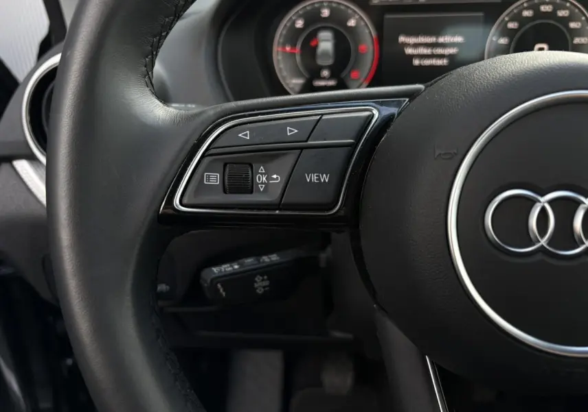 Gros plan sur le volant cuir multifonction noir de l'Audi Q2 30 TDI S-Line avec commandes à gauche et tableau de bord partiel.