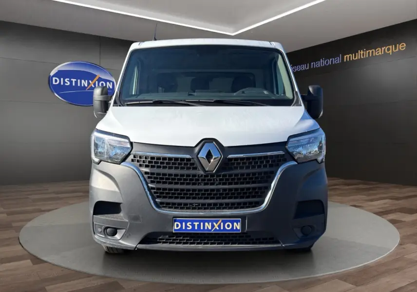 Vue avant d’un utilitaire Renault Master blanc avec calandre noire et logo Renault bien visible, sur fond intérieur showroom.