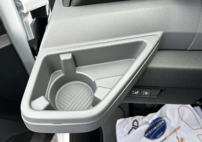 Gros plan sur le porte-gobelet gris intégré côté passager du Renault Master blanc, avec commandes de réglage en arrière-plan.