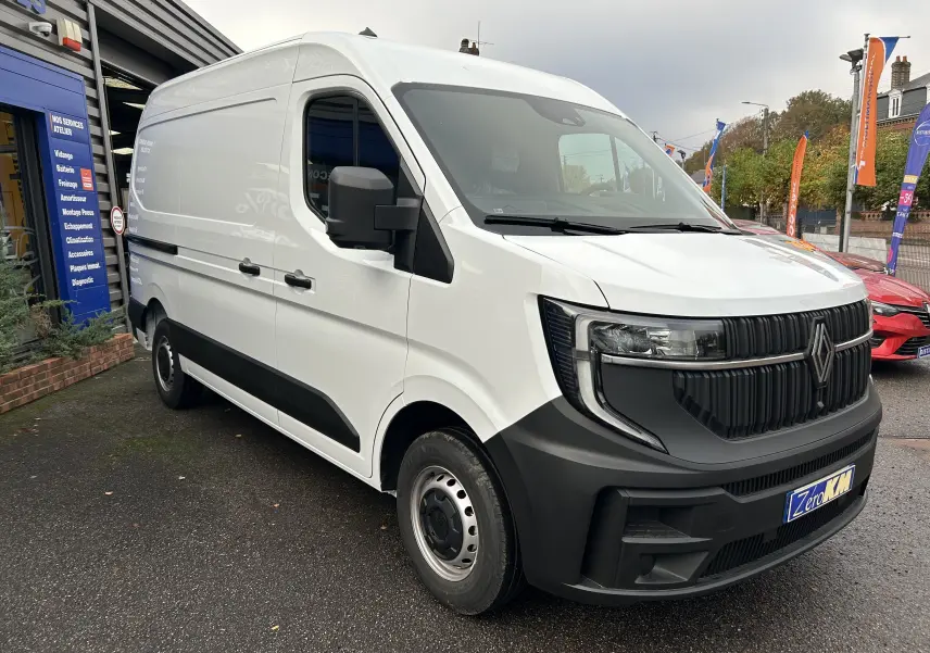Renault Master blanc vu en 3/4 avant droit, avec calandre noire et roues acier, stationné devant un atelier.