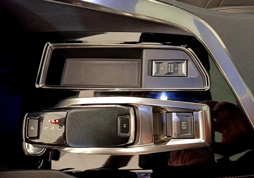 Gros plan sur la console centrale noire brillante du Peugeot 3008 rouge avec levier de boîte auto et bouton Drive Mode.