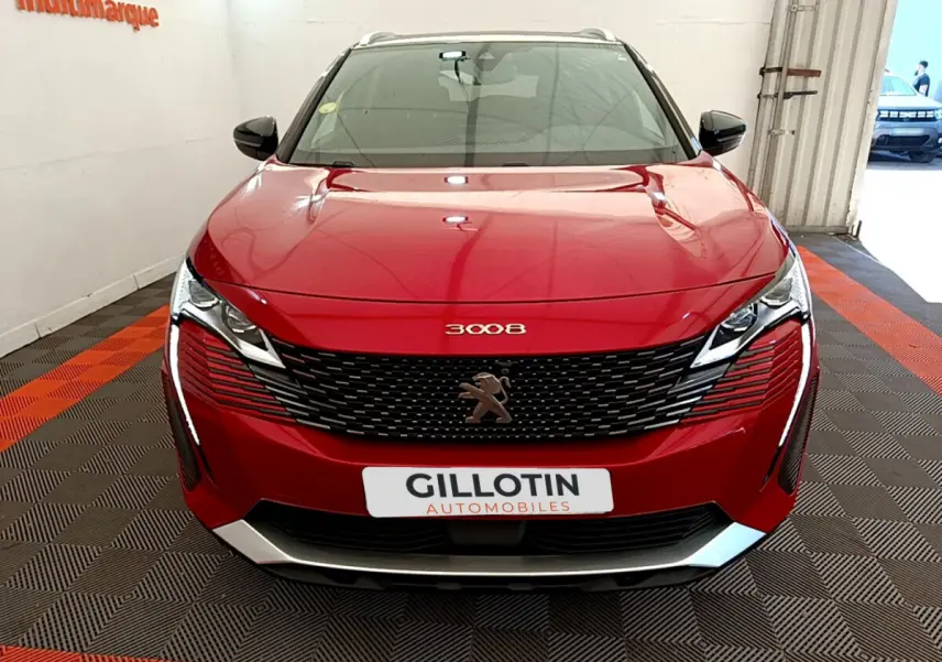 Vue frontale d'un Peugeot 3008 rouge brillant avec calandre noire et logo lion central sur fond de showroom.