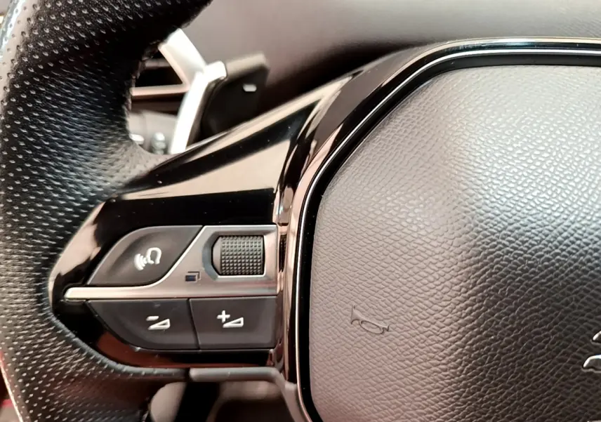 Gros plan sur les commandes gauche du volant en cuir noir du Peugeot 3008 GT rouge, avec boutons multifonctions et molette.