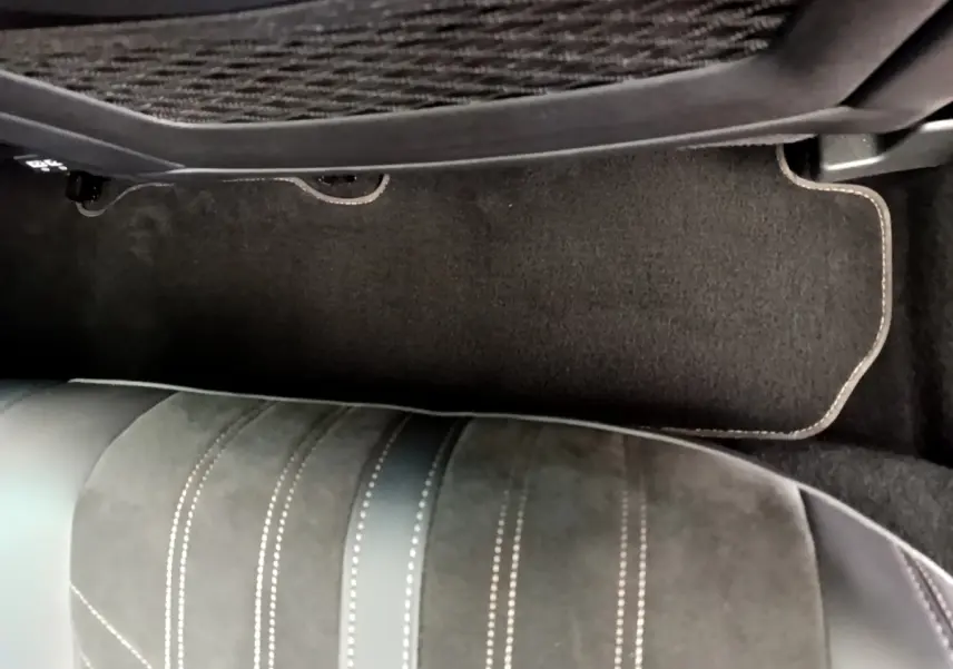 Gros plan sur le tapis de sol et l'assise en cuir noir avec surpiqûres blanches côté passager du Peugeot 3008 GT rouge.