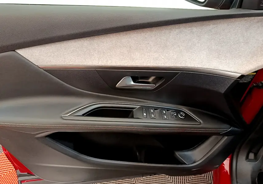 Intérieur côté gauche de la porte d'une Peugeot 3008 rouge, avec commandes de vitres et poignée argentée.