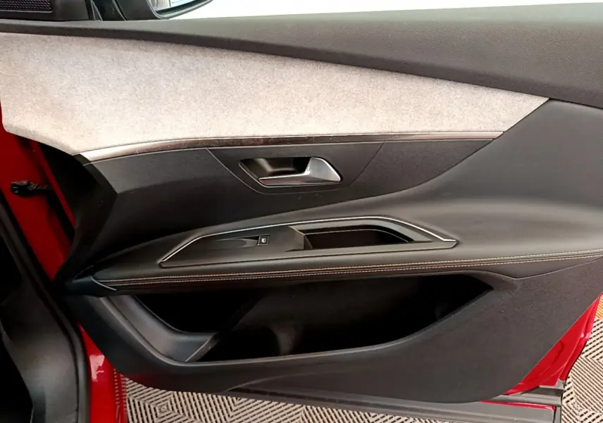 Vue côté gauche de la porte avant rouge du Peugeot 3008 GT avec garniture noire et surpiqûres orange.