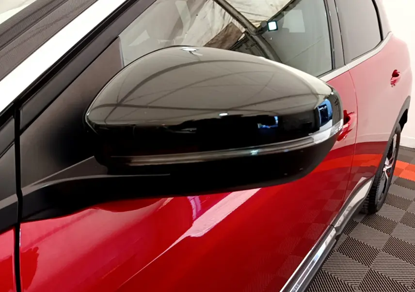 Rétroviseur noir en gros plan côté gauche sur Peugeot 3008 rouge, avec porte et jante partiellement visibles.