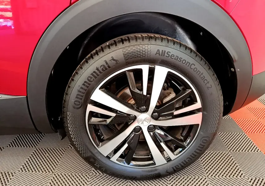 Gros plan sur la roue avant droite d'un Peugeot 3008 rouge, avec jante alliage bicolore et pneu Continental.