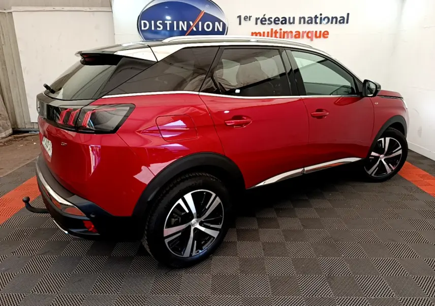 Vue 3/4 arrière droite d'un Peugeot 3008 GT rouge avec jantes alliage et toit noir dans un showroom.