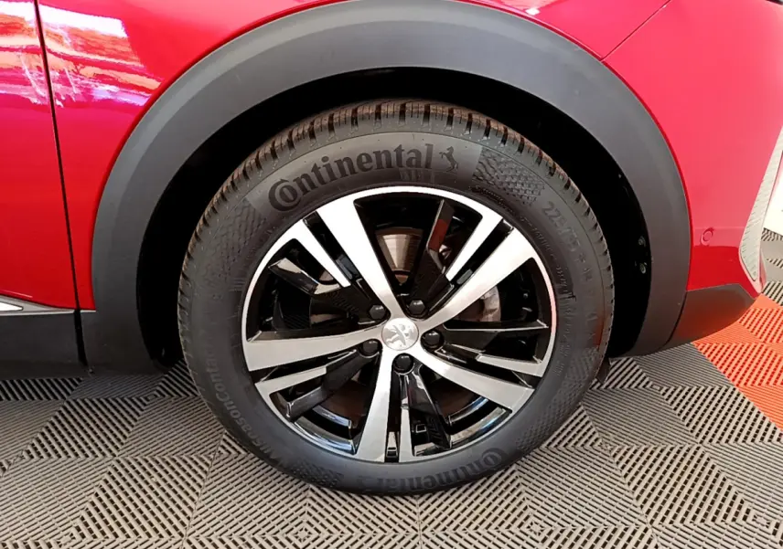 Gros plan sur la roue avant gauche d'un Peugeot 3008 rouge, jante alliage bicolore et pneu Continental.