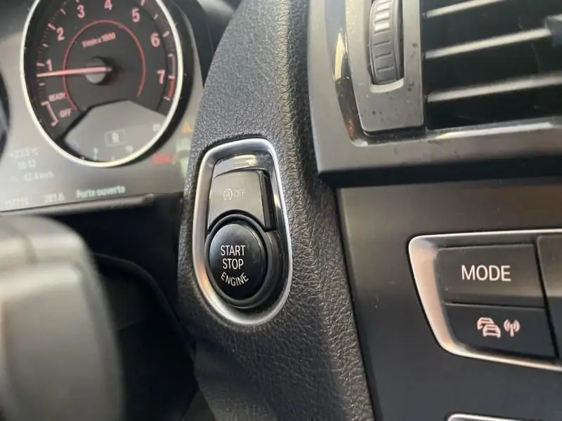 Gros plan sur le bouton Start Stop Engine et le tableau de bord noir d'une BMW Série 1 135i bleu métal de 2013.