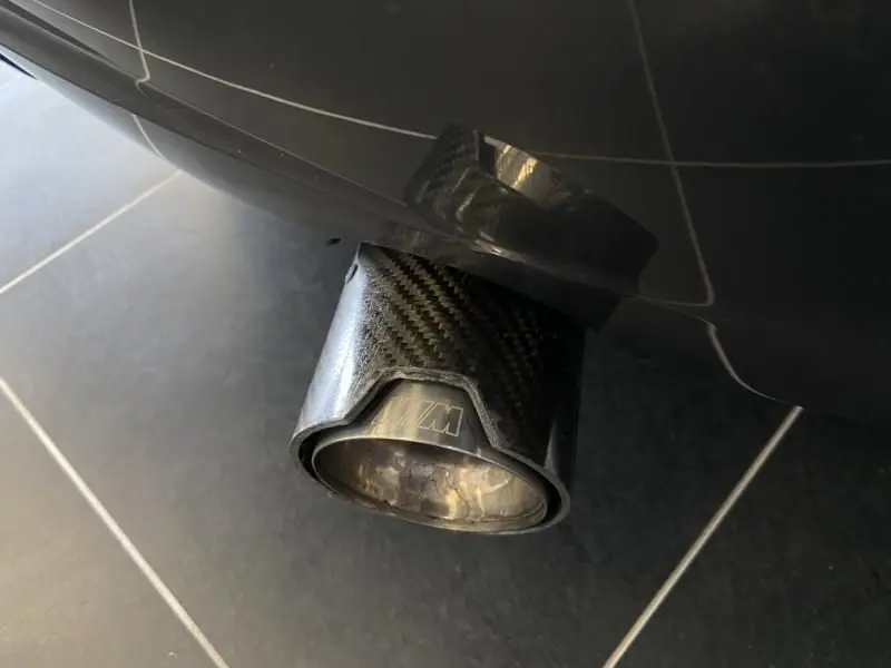 Gros plan sur la sortie d’échappement en carbone avec logo M d’une BMW Série 1 135i bleu métal, vue arrière basse.