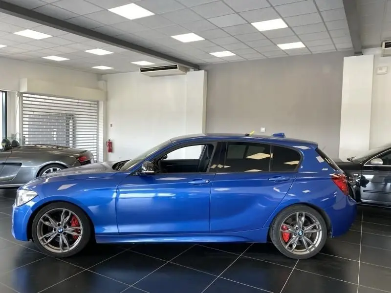 Profil côté gauche d'une BMW Série 1 135i M 2013 bleu métal avec jantes sport et étriers de frein rouges.
