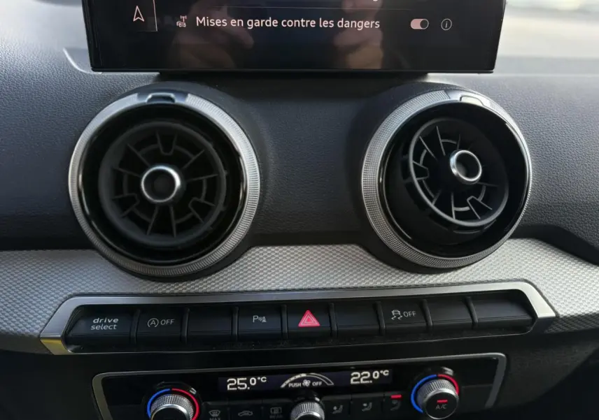 Détail du tableau de bord de l'Audi Q2 30 TDI S-Line 2025, montrant les aérateurs ronds et la commande de climatisation automatique bizona.