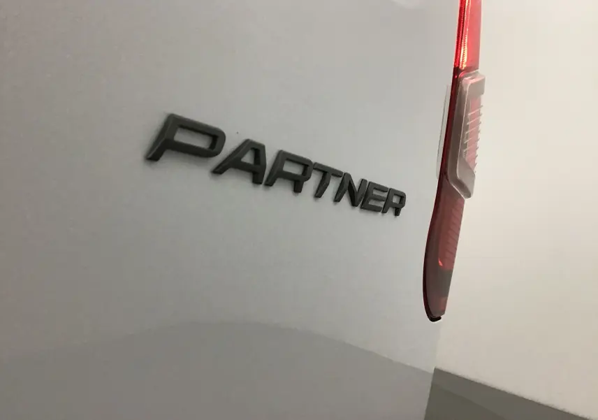 Gros plan sur l'arrière blanc d'un Peugeot Partner avec le logo "PARTNER" et un feu arrière vertical rouge.