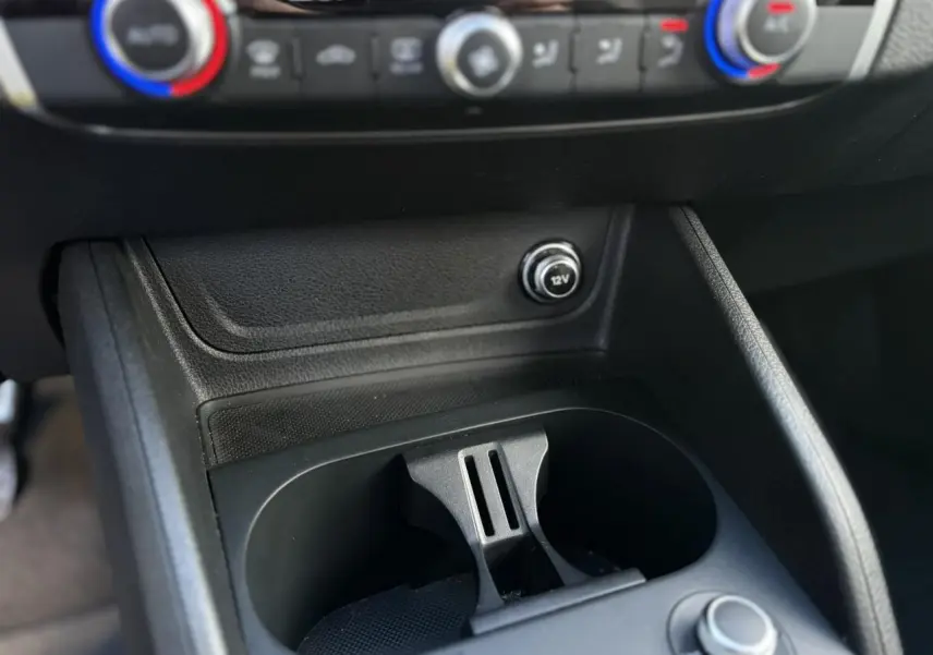 Gros plan sur la console centrale de l'Audi Q2 30 TDI S-Line 2025, montrant les commandes de climatisation et un port 12V.