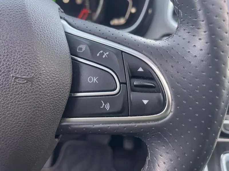 Gros plan sur les commandes multifonctions en cuir perforé du volant côté gauche d'un Renault Espace gris Cassiopée 2018.