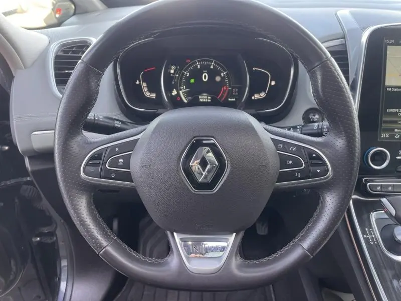 Vue rapprochée du volant cuir noir avec logo Renault et badge Initiale Paris, tableau de bord et écran tactile visibles.