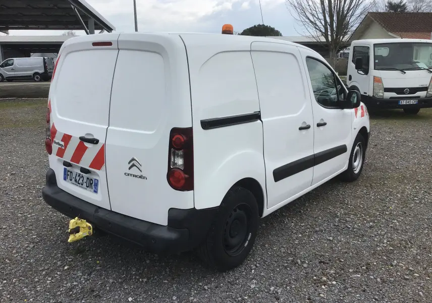 Vue 3/4 arrière droite d’un Citroën Berlingo blanc utilitaire avec bandes rouges réfléchissantes et gyrophare orange.