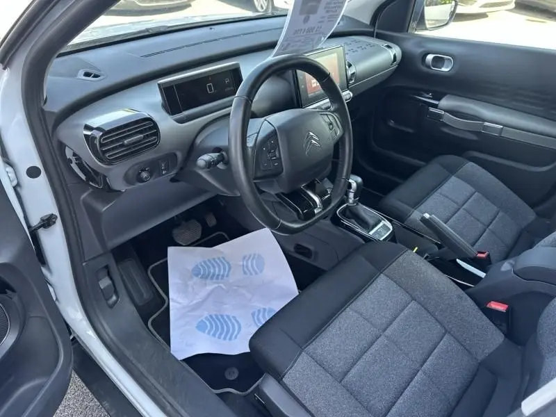Intérieur côté conducteur du Citroën C4 Cactus blanc 2018, avec volant, tableau de bord et sièges gris visibles.