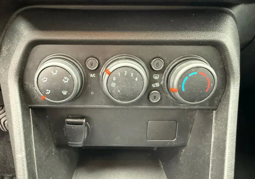 Panneau de commande de climatisation manuelle noir de la Dacia Sandero blanc, avec trois molettes et prise 12V visible.
